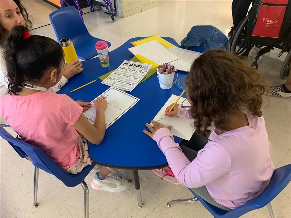  kids sitting at a round blue table working on a school activity